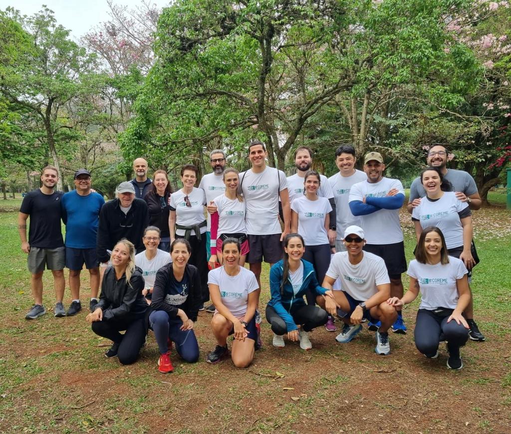 Imagem dos participantes da corrida em um gramado com árvores ao redor.